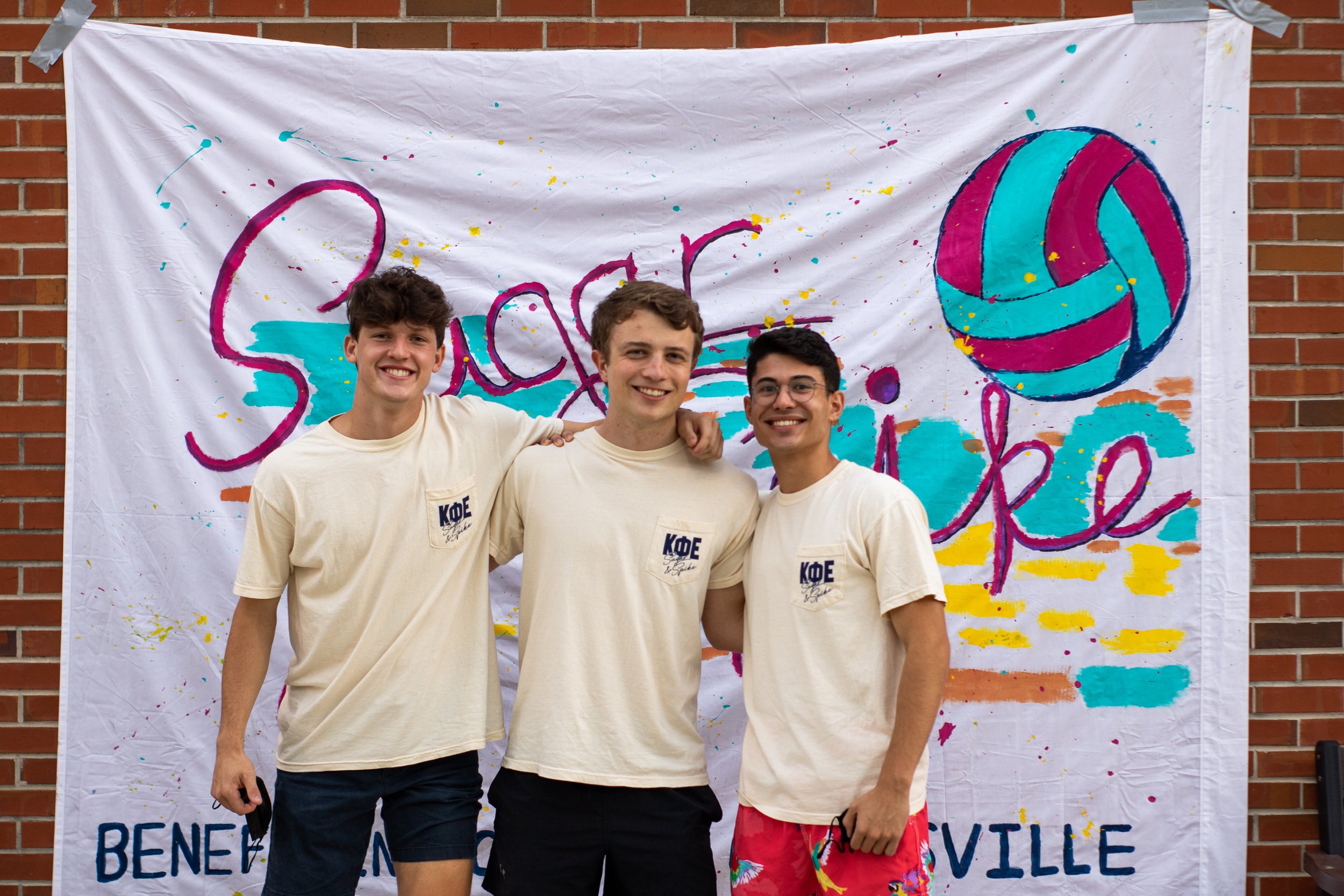 Three Kappa Phi Epsilon brothers in front of the Sugar and Spike event banner